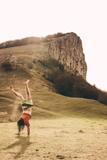 This image shows a person performing a handstand on a grassy slope near a rocky mountain. The scene captures the essence of adventure, fitness, and connection with nature. Ideal for use in travel blogs, adventure magazines, fitness inspiration, and outdoor activity promotions.