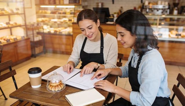 Baristas reviewing schedule and inventory at cozy bakery table