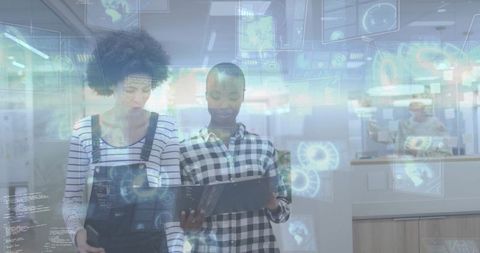 Two coworkers reviewing holographic data dashboards in modern office wearing overalls and checked sh