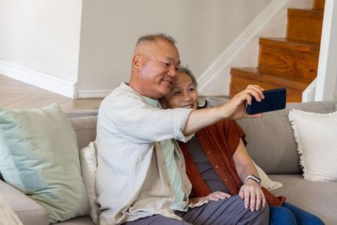 Senior couple sitting on couch taking selfie with smartphone showing warm companionship