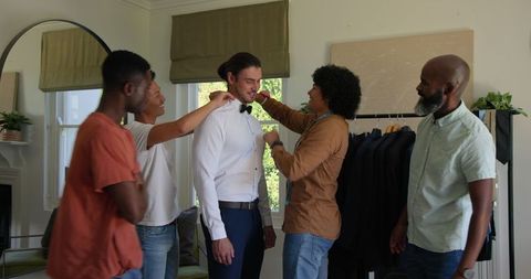 Groomsmen assisting groom with bow tie in dressing room