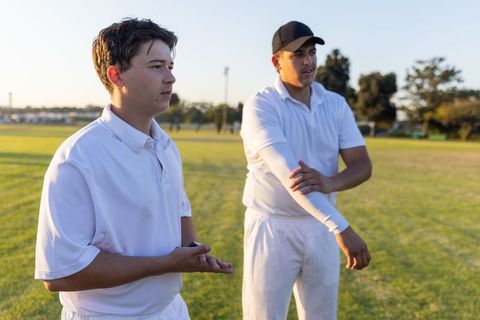 Two cricketers preparing for match during golden hour on grassy field showing focus