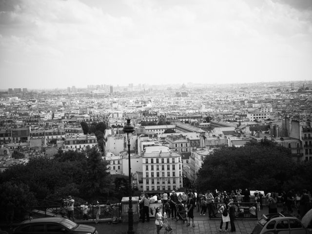 Black and white panoramic view of Paris from Montmartre. Urban cityscape featuring notable architecture, with buildings stretching into the horizon. Tourists gathering on a viewpoint, adding liveliness to the historic city atmosphere. Suitable for designs focusing on travel, tourism, European cities, historic landmarks, and urban exploration.