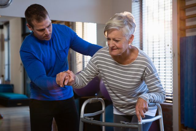 Physiotherapist helping senior woman with walking frame in a clinic, suggesting a focus on rehabilitation and elderly care. Suitable for use in health care, physical therapy, and rehabilitation service promotions. Use in articles or advertisements about patient support, mobility aid, and senior care.