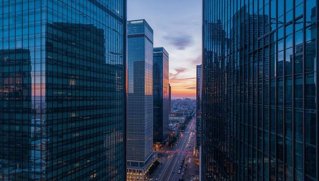Framing urban corridor between glass skyscrapers reflecting sunset over multi-lane avenue