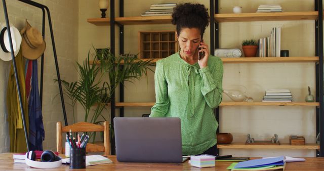 Biracial woman using laptop and talking on smartphone while working from home - Download Free Stock Photos Pikwizard.com