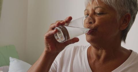 Senior Woman Drinking Water and Taking Medicine in Comforting Setting