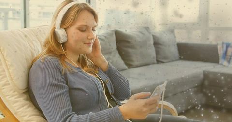 Young woman relaxing and listening to music with wired headphones on sunlit armchair
