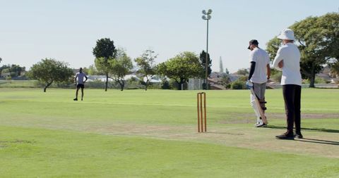 Playing casual suburban cricket on sunny pitch with batsman and bucket-hat teammate