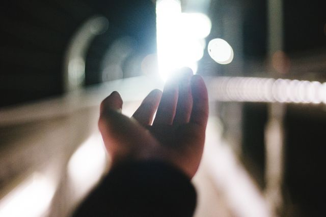 Hand reaching out towards a bright light in a modern, futuristic tunnel. The blurred background and strong light create a sense of aspiration, hope, and journey towards the unknown. Ideal for illustrating concepts of ambition, dreams, and the emotional journey towards goals. Useful for motivational imagery, blog posts, and inspirational content.