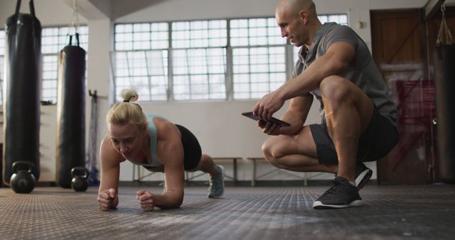 Fit caucasian woman performing plank exercise with male trainer holding digital tablet at the gym. sports, training and fitness concept