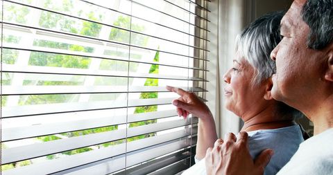 Senior Asian Couple Looking Out Window with Hopeful Expressions