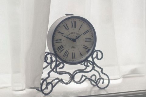 Vintage roman numeral table clock against white curtain