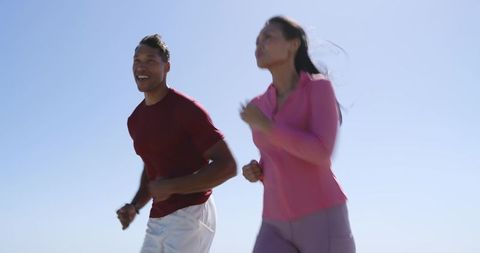 Mid-Adult Couple Jogging on Coastal Trail Under Clear Blue Sky