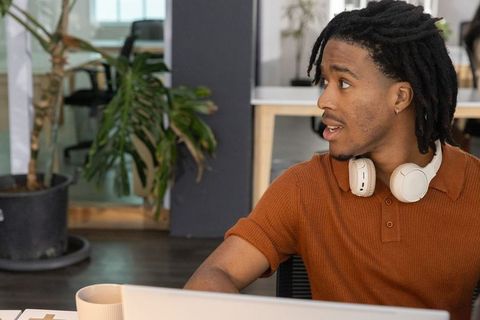 Young man working at coworking desk wearing headphones collaborating in modern office