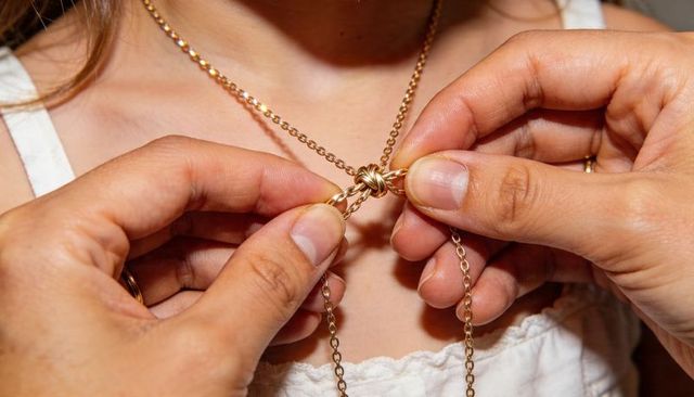 Fastening gold knot necklace closeup showing gentle hands adjusting jewelry at collarbone