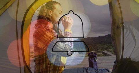 Woman sipping coffee in tent on wooden deck overlooking valley and mountains during overcast morning