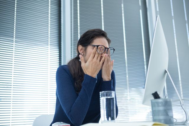 Tired female executive rubbing her eyes at desk in office