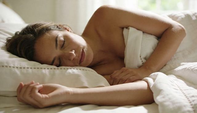 Peaceful woman sleeping on side in white sheets under soft morning light