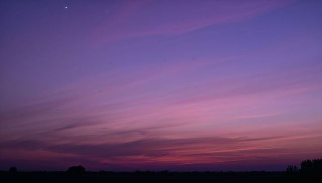 Glowing twilight sky painting pink and purple layered clouds over rural horizon