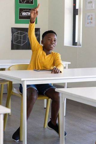 African american preteen raising hand in classroom while holding tablet learning math
