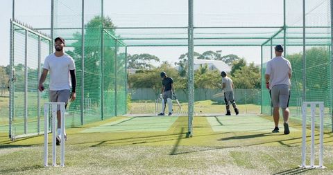 Outdoor cricket nets team training batting and bowling practice with diverse players