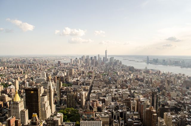 This image captures an aerial view of the densely packed Manhattan skyline, emphasizing both classic and modern skyscrapers along with the flowing Hudson River in the background. This could be ideal for travel promotions, real estate advertisements, urban planning presentations, and New York City-themed websites and blogs.