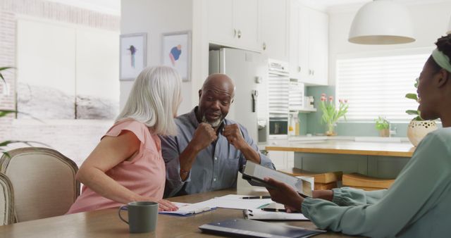 Senior couple sitting with financial advisor in a bright, modern kitchen, discussing financial plans and reviewing documents. Ideal for portraying financial advisory services, senior lifestyle, retirement planning, and home consultation services. Emphasizes teamwork, communication, and professional guidance for financial well-being.