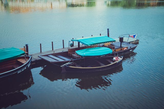 Two traditional boats are docked on a calm lake with green canopies covering them. The water is tranquil, reflecting the boats. This can be used for themes involving travel, nature, transportation, outdoor activities, and serene environments. Ideal for websites, travel brochures, and nature blogs.