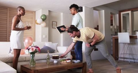 Friends Gather Around Table Arranging Cake and Drinks at Indoor Party