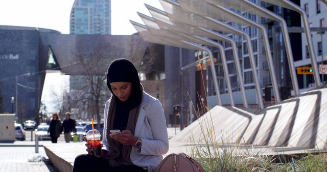 Muslim woman using smartphone while having a beverage outdoors in urban setting - Download Free Stock Images Pikwizard.com