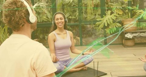 Couple meditating with headphones in tropical sunroom greenhouse yoga and mindfulness practice