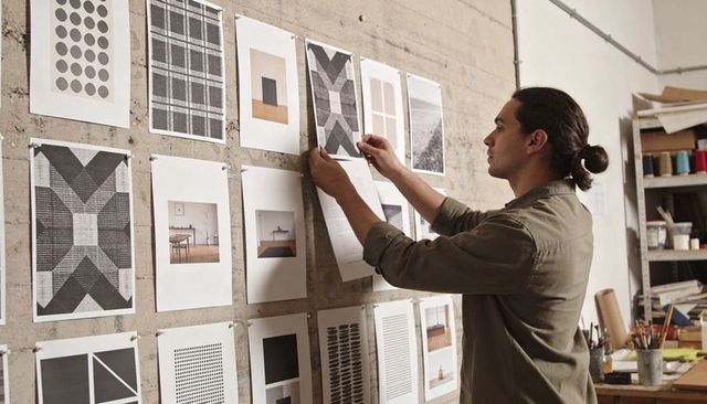 Man arranging graphic prints on concrete wall in design studio for layout review