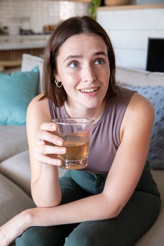 Young Woman Relaxing on Sofa with Refreshing Glass Drink