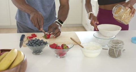 Couple preparing nutritious breakfast with fresh berries, yogurt and oats on countertop