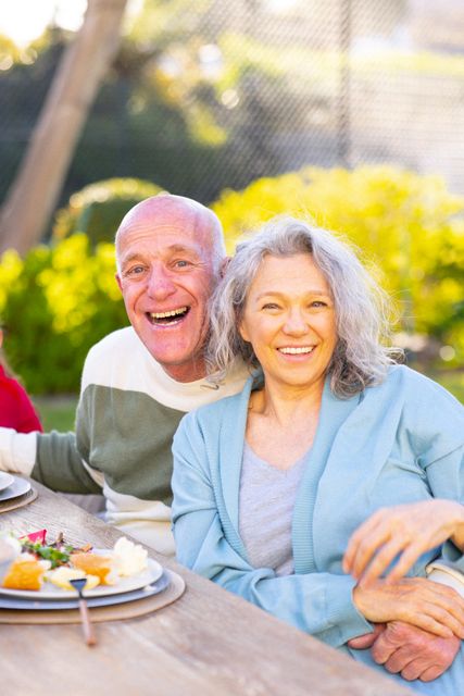 Vertical portrait of happy caucasian grandparents during meal at table in garden, copy space. Family, togetherness, domestic life and happiness concept.