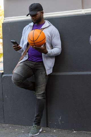 Street basketball player checking phone while leaning against urban wall