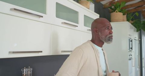 Senior african american man enjoying morning coffee in modern kitchen with plants and neutral decor