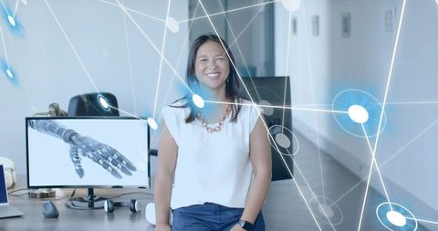 Smiling Engineer in Modern Office with Robotic Hand on Monitor