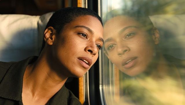 Contemplative young woman gazing from train window with reflective portrait and sunlight
