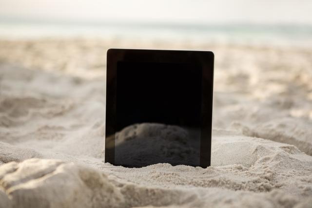 Digital tablet standing upright in sandy beach environment. Ideal for concepts related to technology use during vacations, outdoor relaxation, summer travel, and digital lifestyle. Can be used in travel blogs, tech advertisements, and summer vacation promotions.