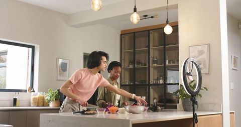 Cohosts filming cooking tutorial, chopping and mixing at modern kitchen island