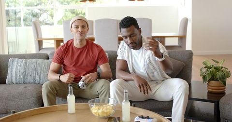 Diverse Friends Playing Video Games on Couch Sharing Chips and Drinks Casual Gaming