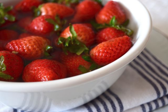 Vibrant, red strawberries are soaking in a white bowl filled with water, indicating they are being prepared for consumption by cleaning. The close-up shot emphasizes freshness and natural colors. Ideal for use in healthy eating promotions, recipe blogs, magazine articles on organic and farm fresh produce, and diet-related content.