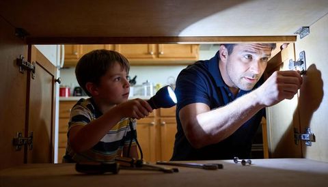 Father and son repairing kitchen cabinet with flashlight and wrench, teaching hands-on diy skills