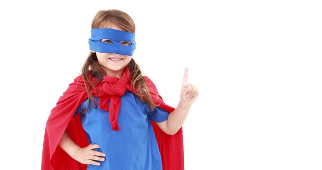 Happy caucasian preschool girl in red cape and blue mask, pointing finger on white background. Children, childhood, playing time and preschool activities,disguises, unaltered.