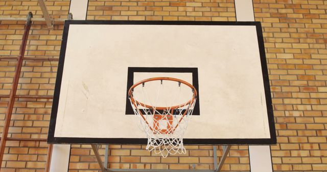 A basketball hoop is mounted against a brick wall backdrop, with copy space. The net and orange rim contrast with the geometric patterns of the bricks, emphasizing the sporty setting.