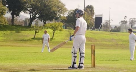 Batsman ready on grassy cricket pitch during daytime match