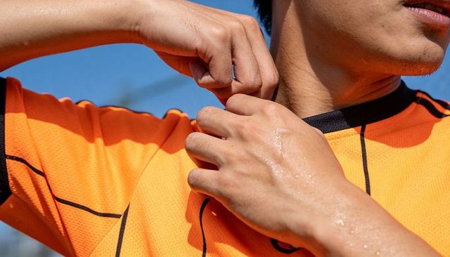 Adjusting orange jersey collar, sweaty male athlete preparing for match on sunlit field
