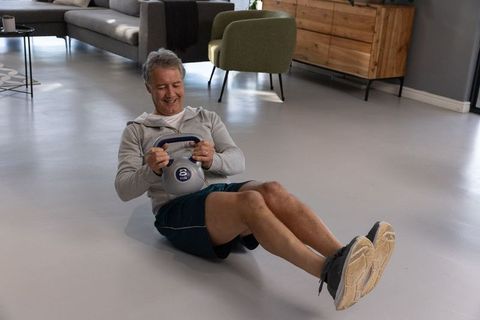 Senior man exercising with kettlebell in living room